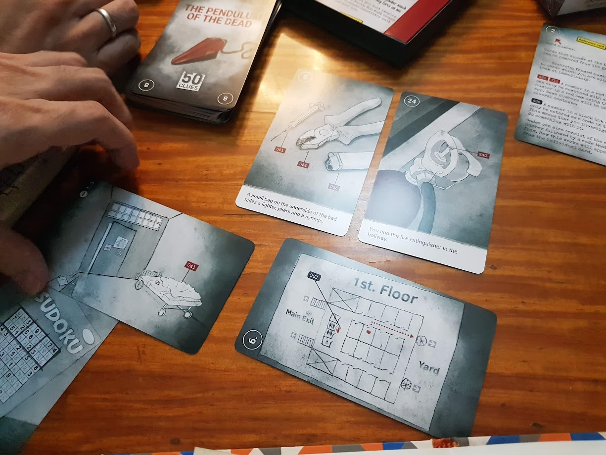 Gameplay photo of the board game 50 Clues: The Pendulum of the Dead featuring various components and board state.