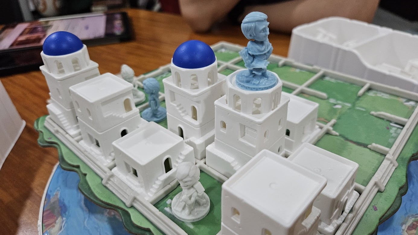 Gameplay photo of the board game Santorini: Pantheon Edition featuring various components and board state.