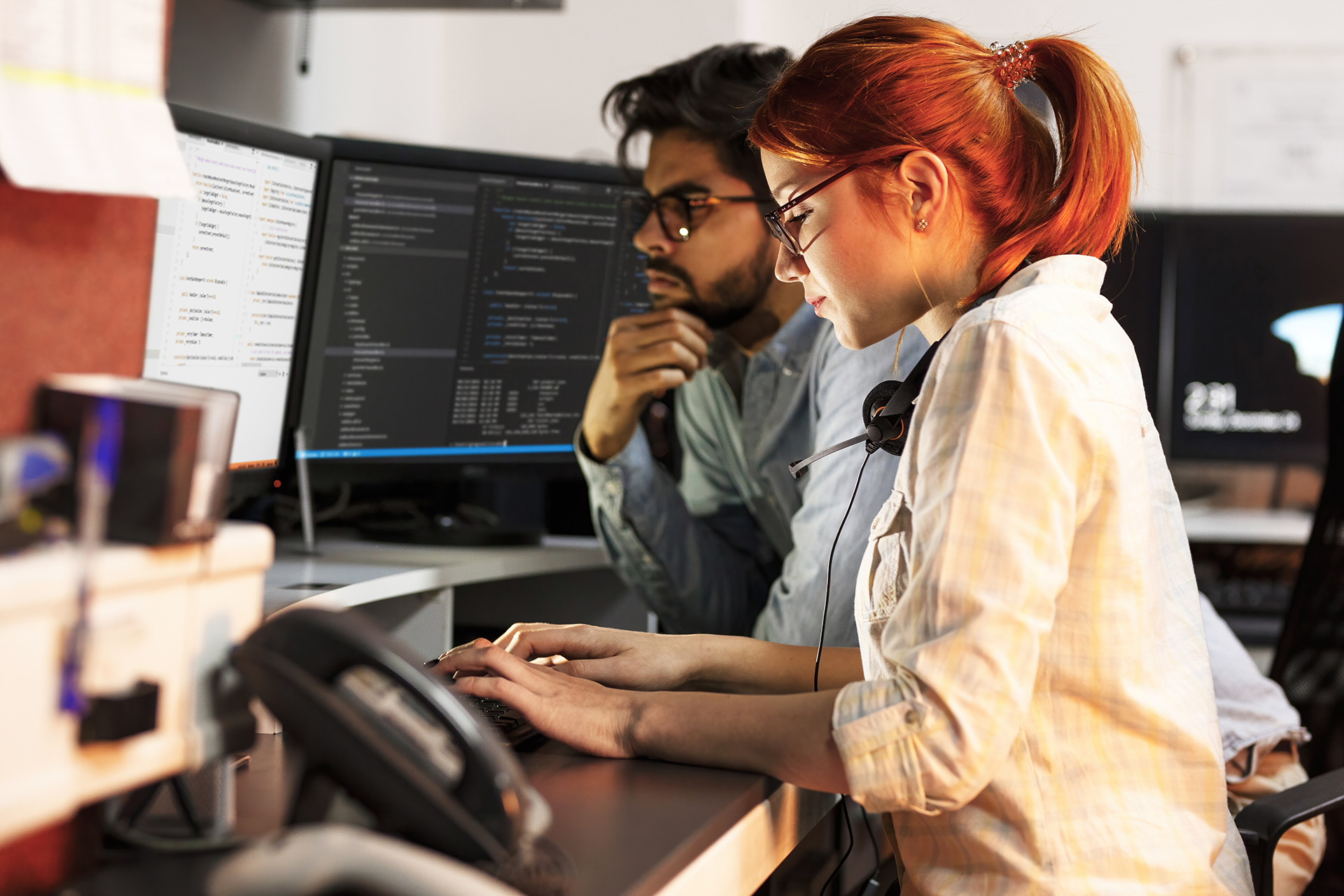 Two programmers working late at night on coding projects displayed on dual monitors in an office.