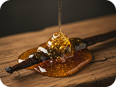 Honey dripping from a wooden honey dipper onto a wooden surface.