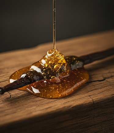 Close-up of golden honey dripping onto a vanilla bean pod on a wooden surface.