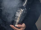 Person holding a clear glass bottle labeled 'BLACK' surrounded by smoke or fog.