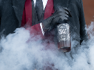 Person in formal attire with black gloves holding a smoking glass bottle with skull and flames design.