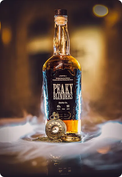 Bottle of Peaky Blinders whiskey with a vintage pocket watch on a smoky surface against a blurred warm background.