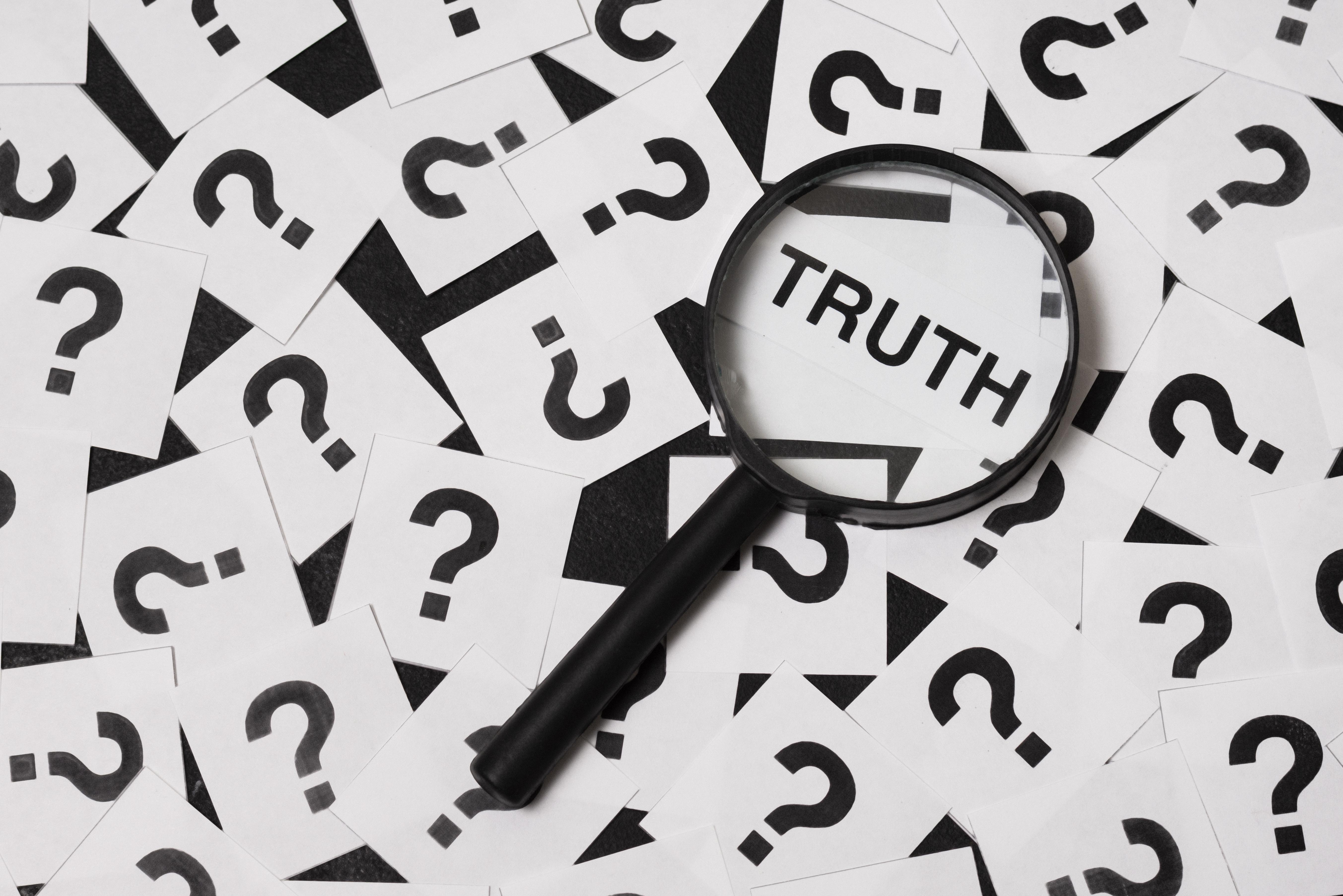 Truth uncovered under a magnifying glass surrounded by scattered question marks, symbolising investigation, uncertainty, fact-checking, myths, misinformation, or searching for clarity and answers.