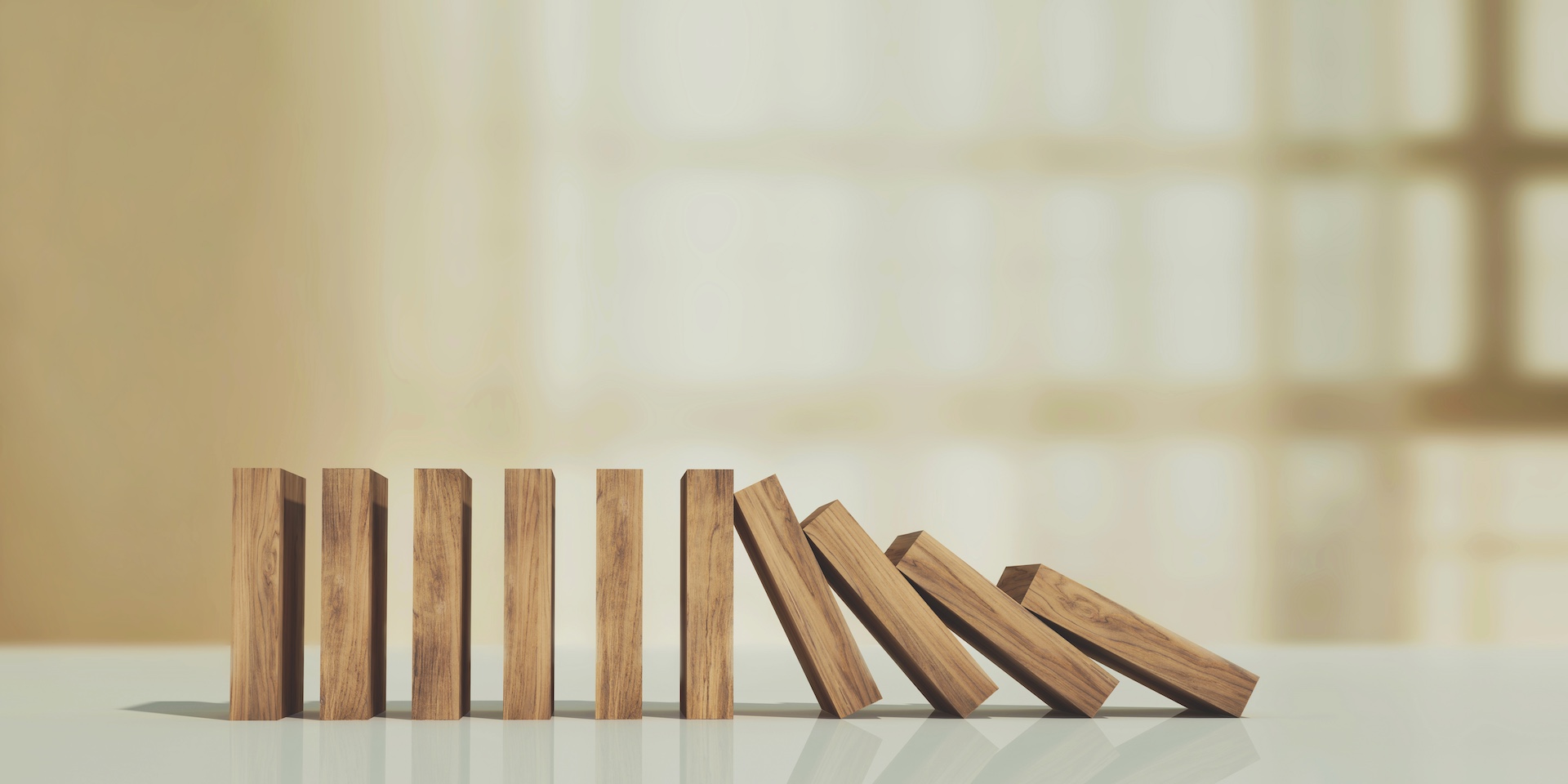 Wooden domino blocks standing and falling in sequence, symbolising escalating risk, chain reactions, unintended consequences, compliance failures, professional negligence or how one issue can trigger wider problems.