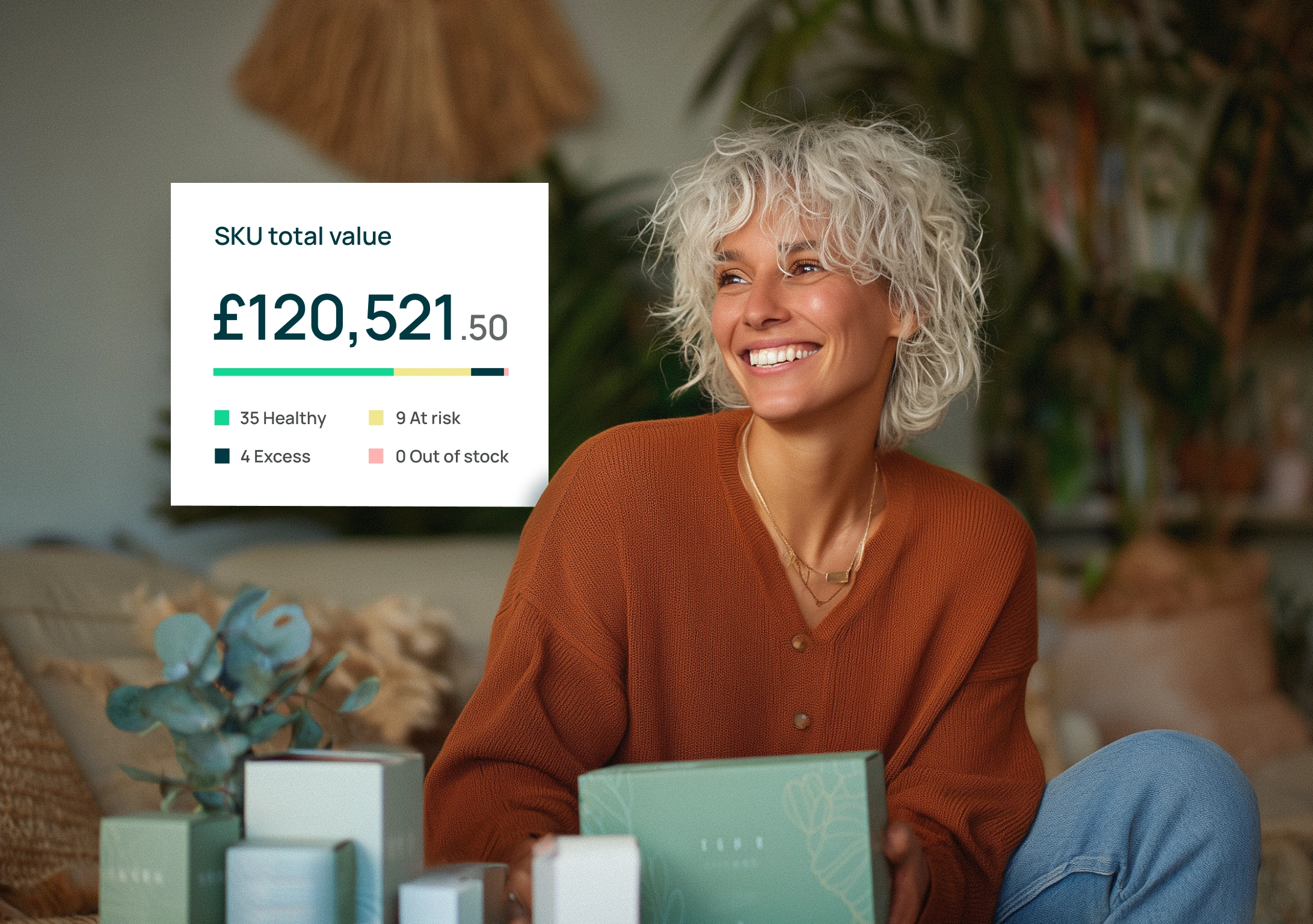 Smiling woman with curly platinum hair wearing an orange sweater, sitting with green product boxes and a graphic showing SKU total value of £120,521.50 including stock status breakdown.