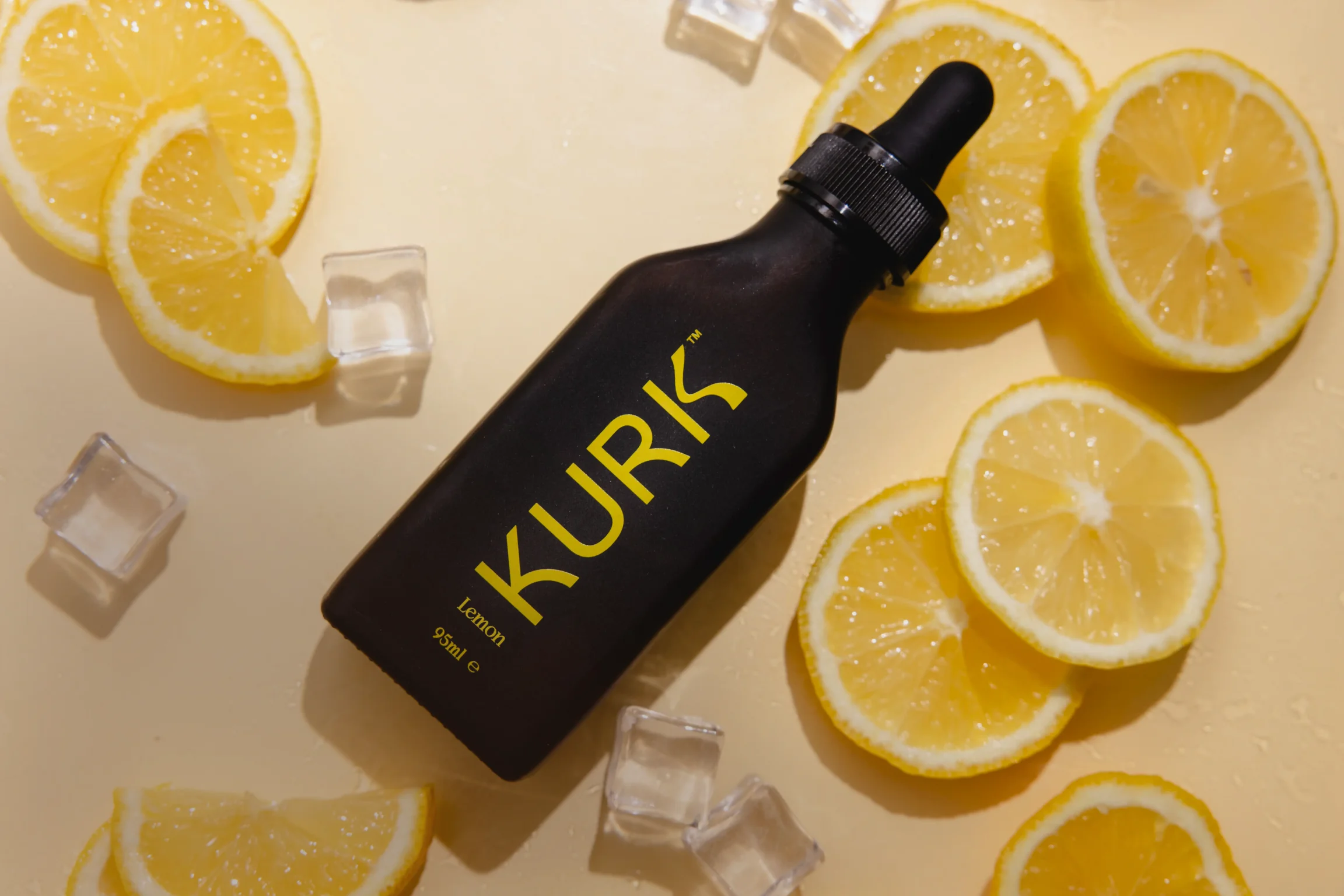 Black dropper bottle labeled 'KURK Lemon 95ml' surrounded by lemon slices and ice cubes on a light surface.