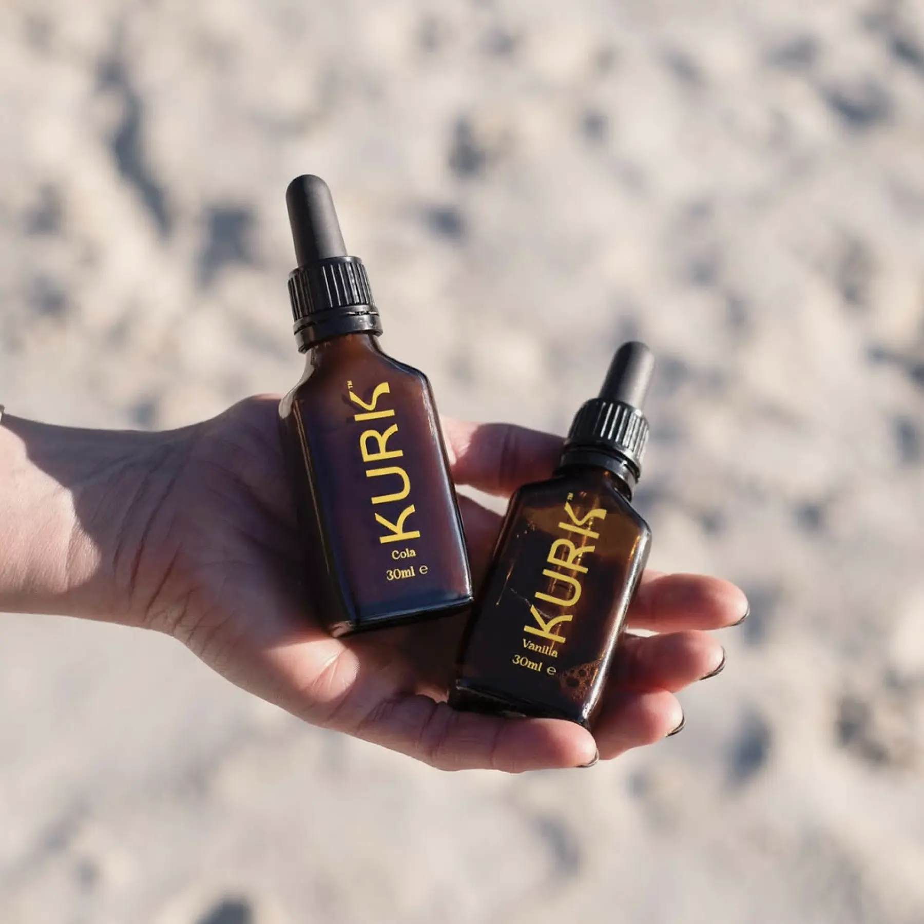 KURK product bottles being held in palm of hand above sandy background