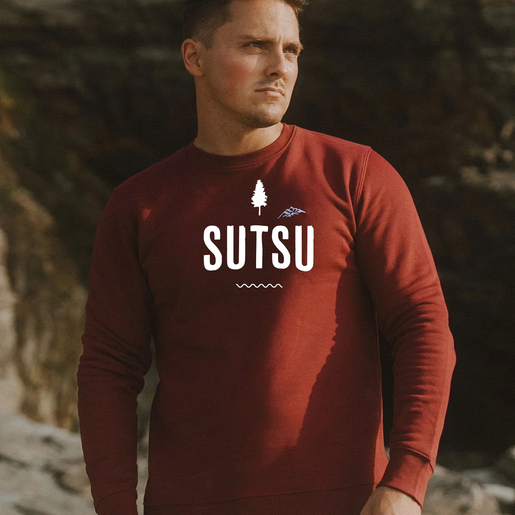 SUTSU logo above image of man wearing SUTSU jumper in bucolic outdoor setting