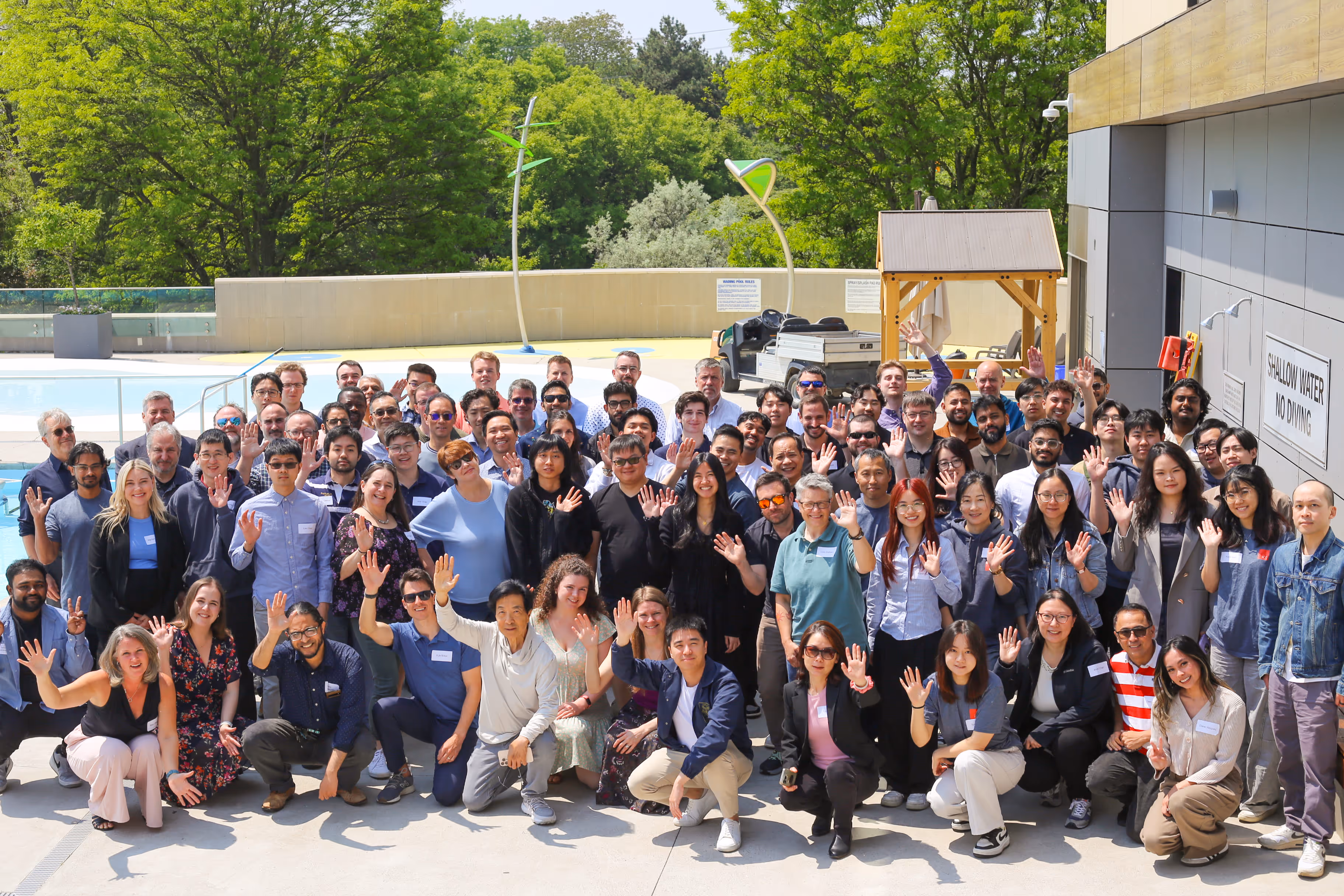 ComputerTalk team posing outdoors, waving and smiling at the camera on a sunny day.