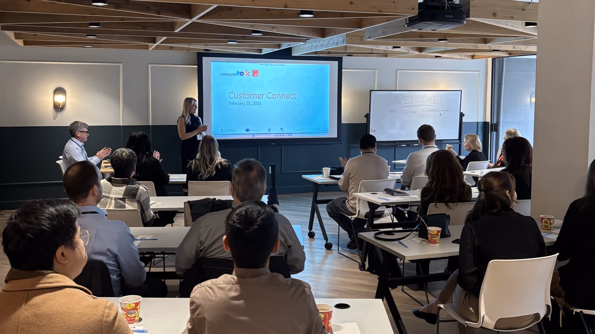 Audience in a modern room listening to a woman presenting at a Customer Connect event on February 25, 2025.