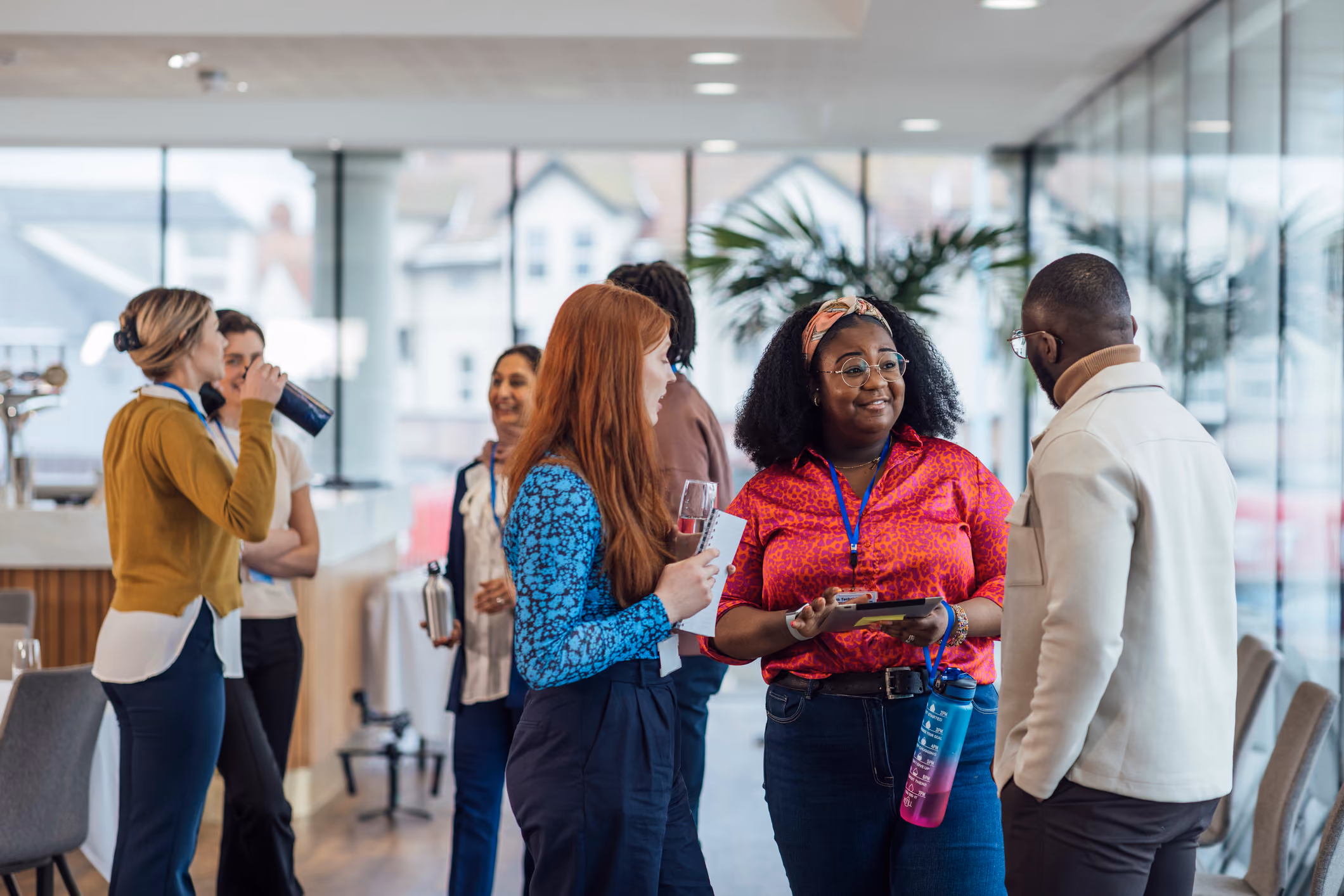 Diverse professionals chatting in a bright modern office with large windows and plants.
