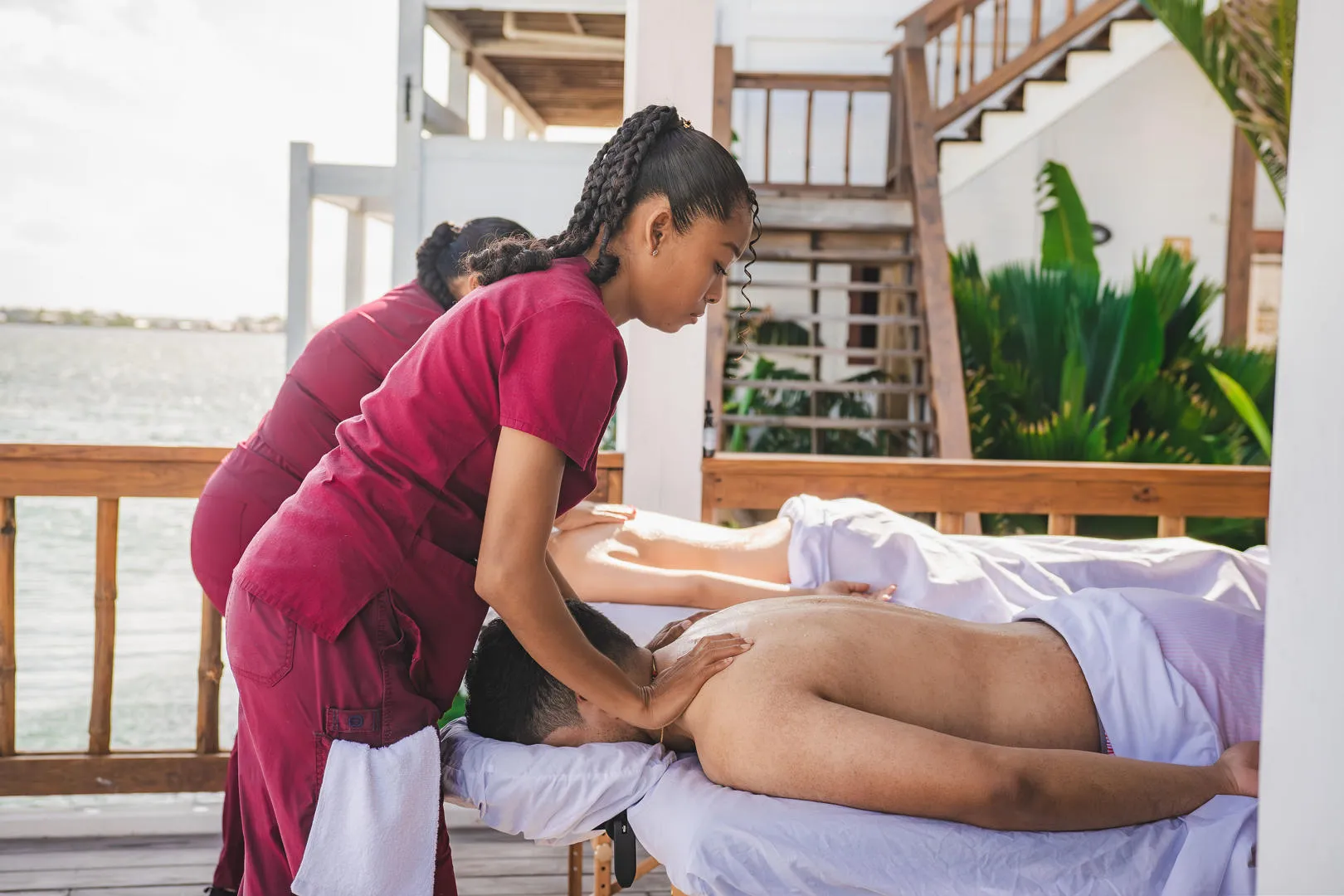 Two people receiving outdoor massages on a deck overlooking the water.