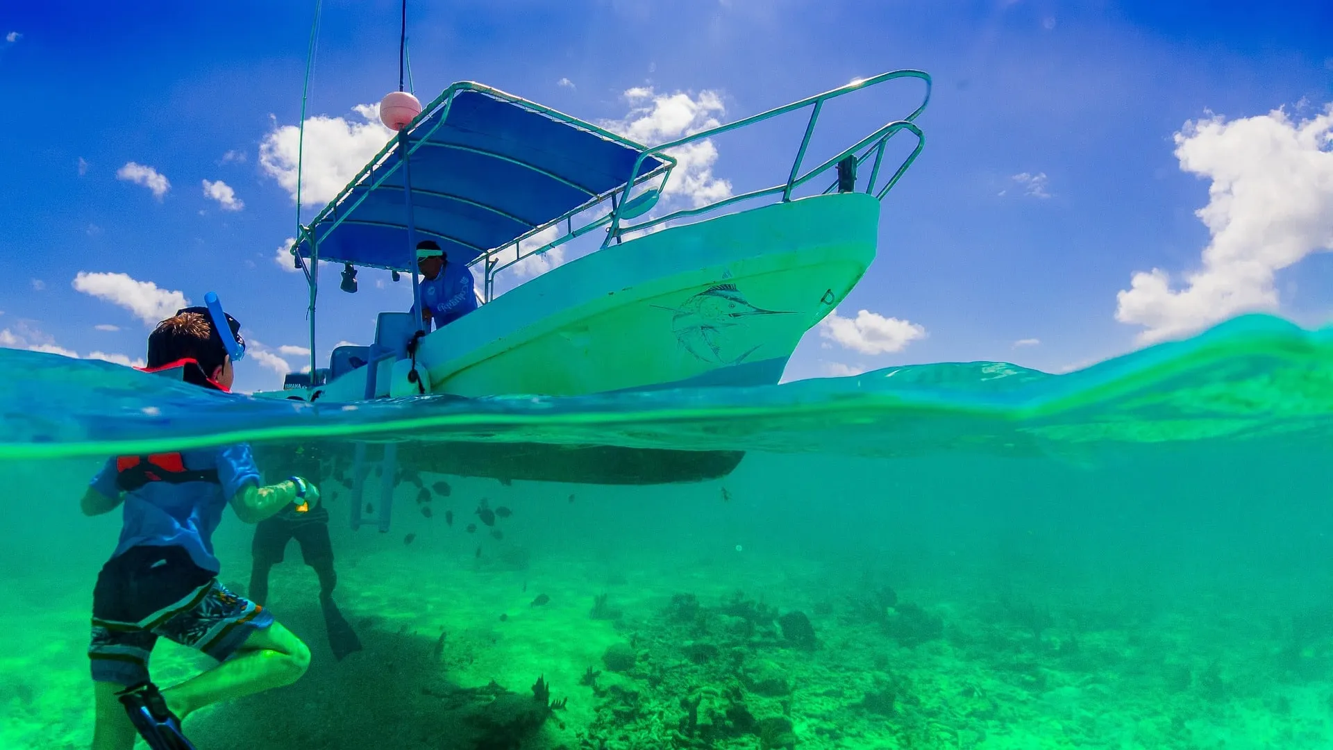 Snorkeler in clear water near a small boat with a guide above.