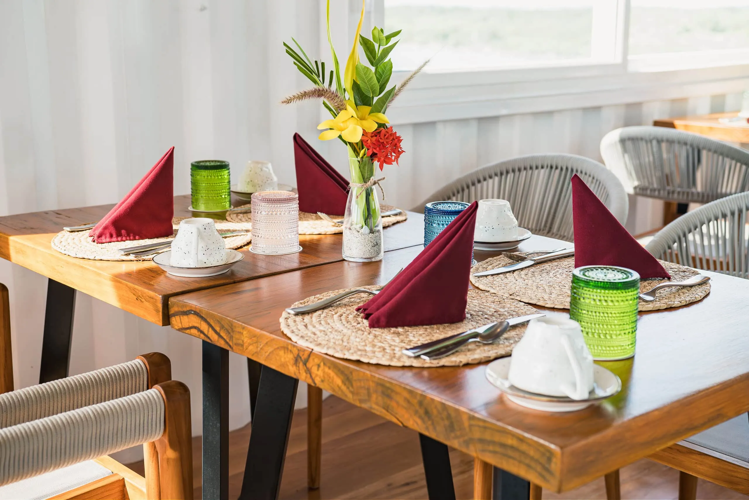 Wooden dining table set with place settings, folded red napkins, and a floral centerpiece.