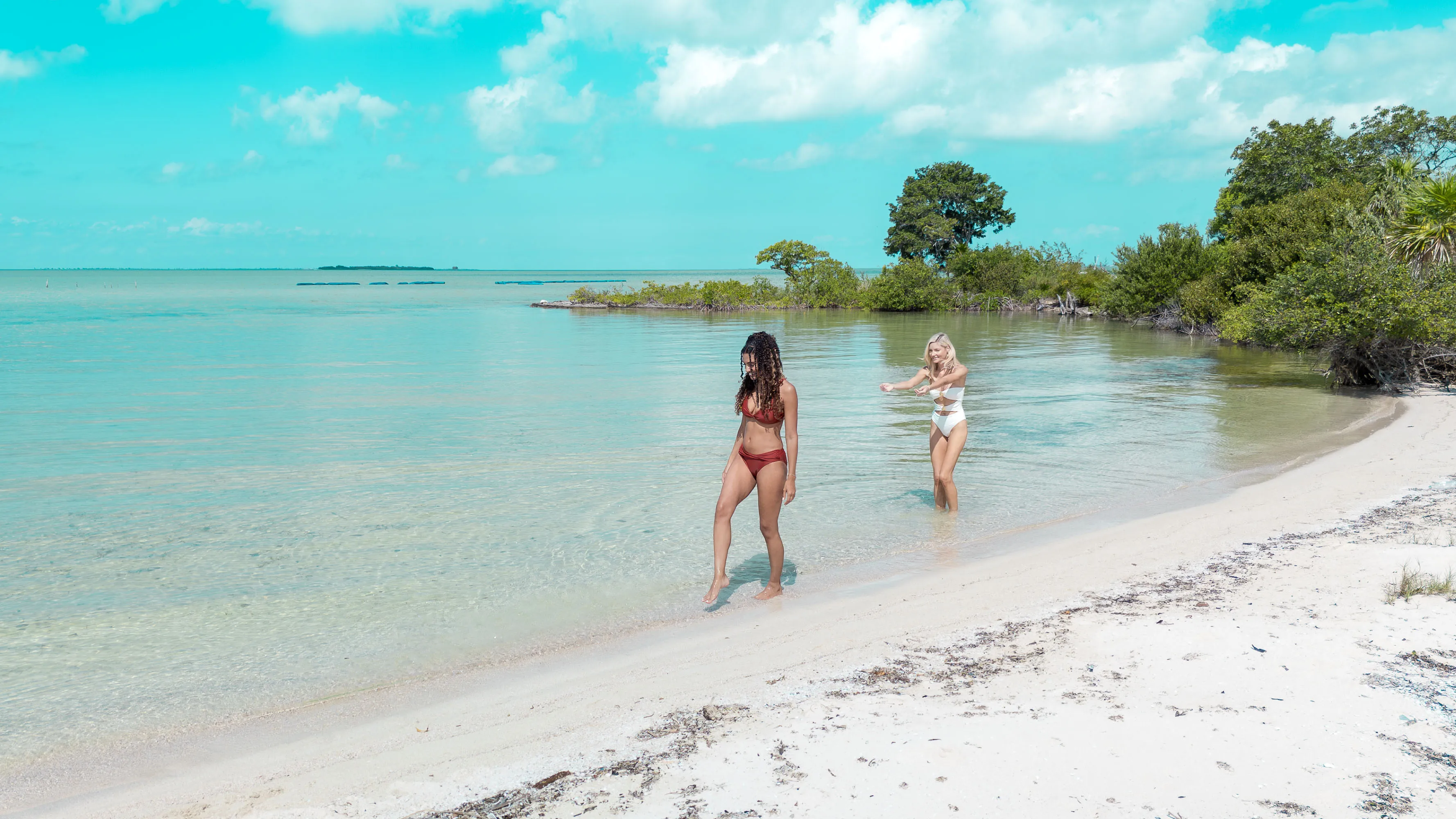Two women enjoying a peaceful beach walk along clear turquoise water