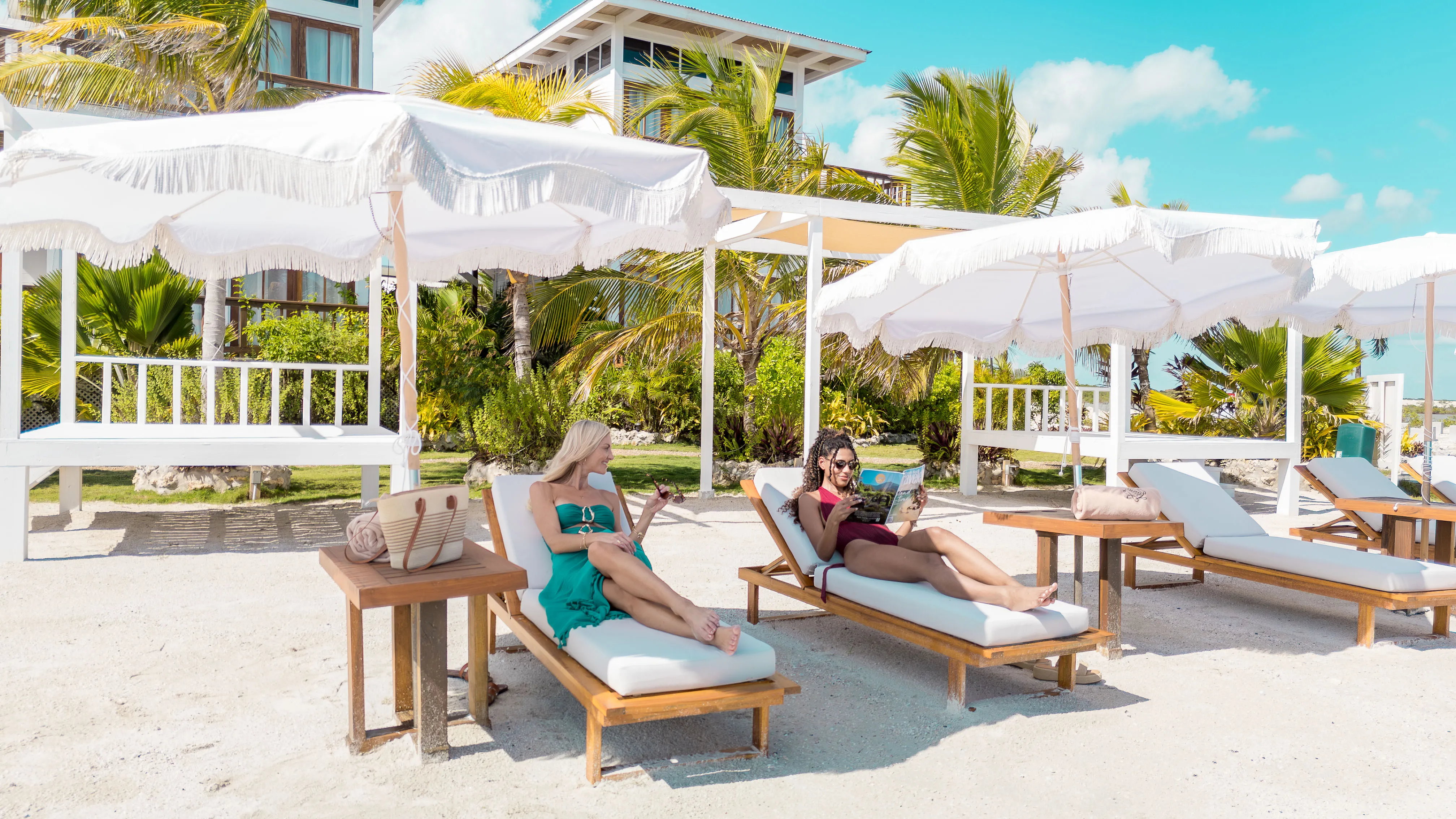 Two women relaxing on beach loungers under white umbrellas at resort