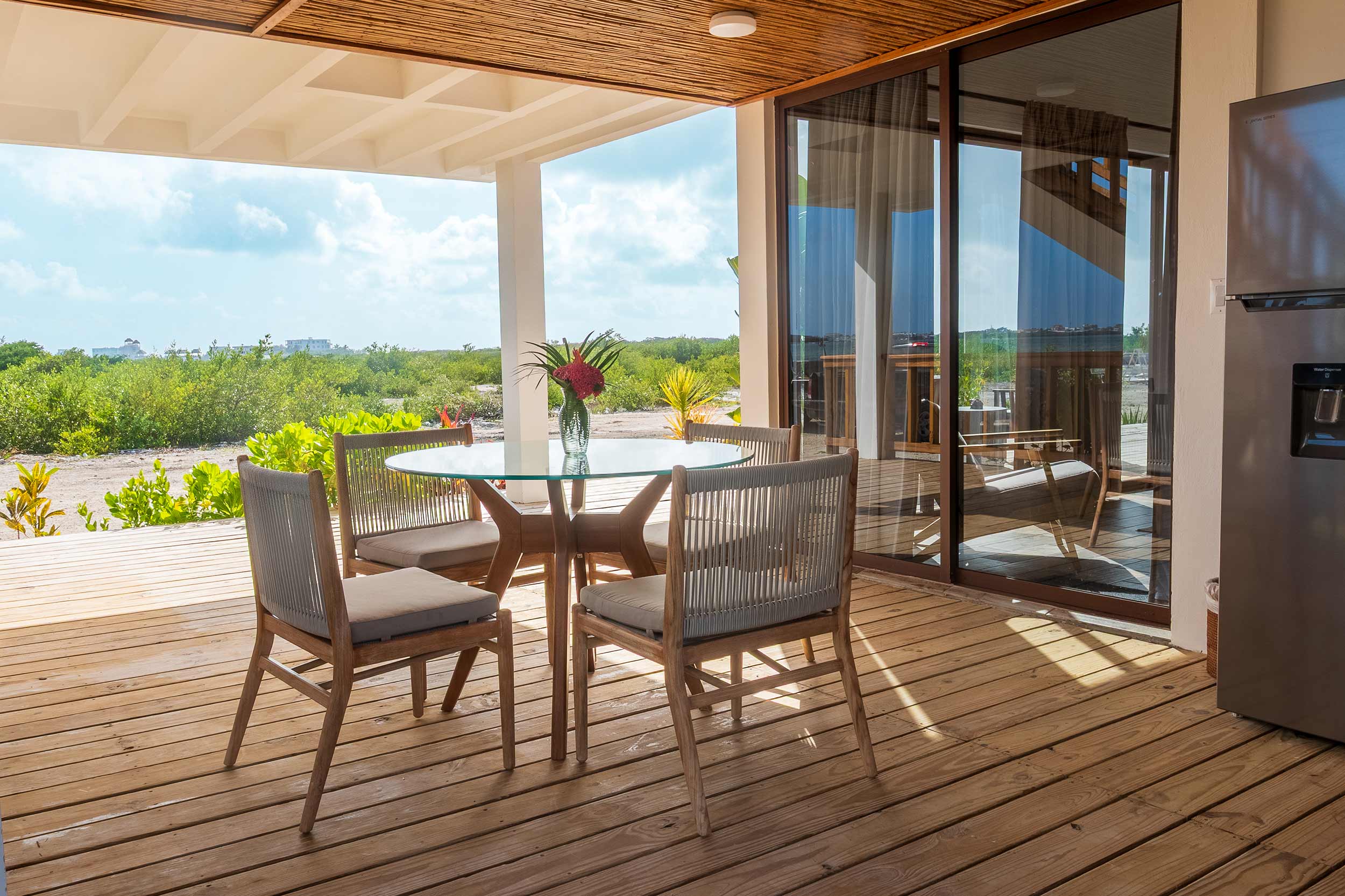 Open-air patio with round dining table and chairs overlooking lush mangroves and coastal scenery.
