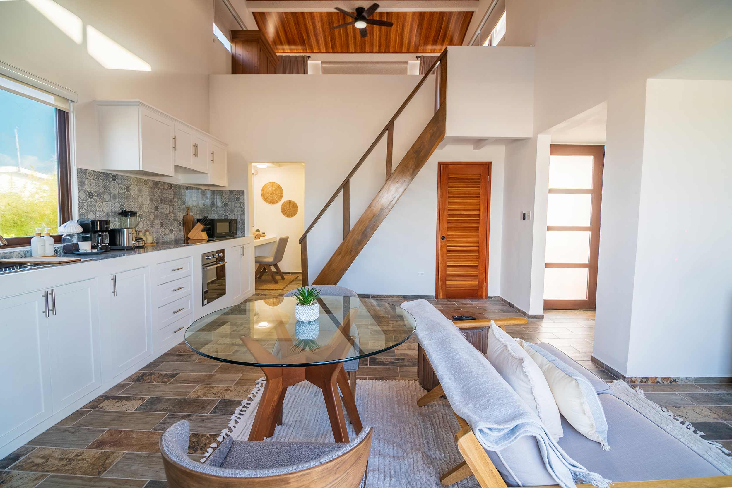 Villa kitchen and dining area featuring patterned tile backsplash and wooden staircase to loft.