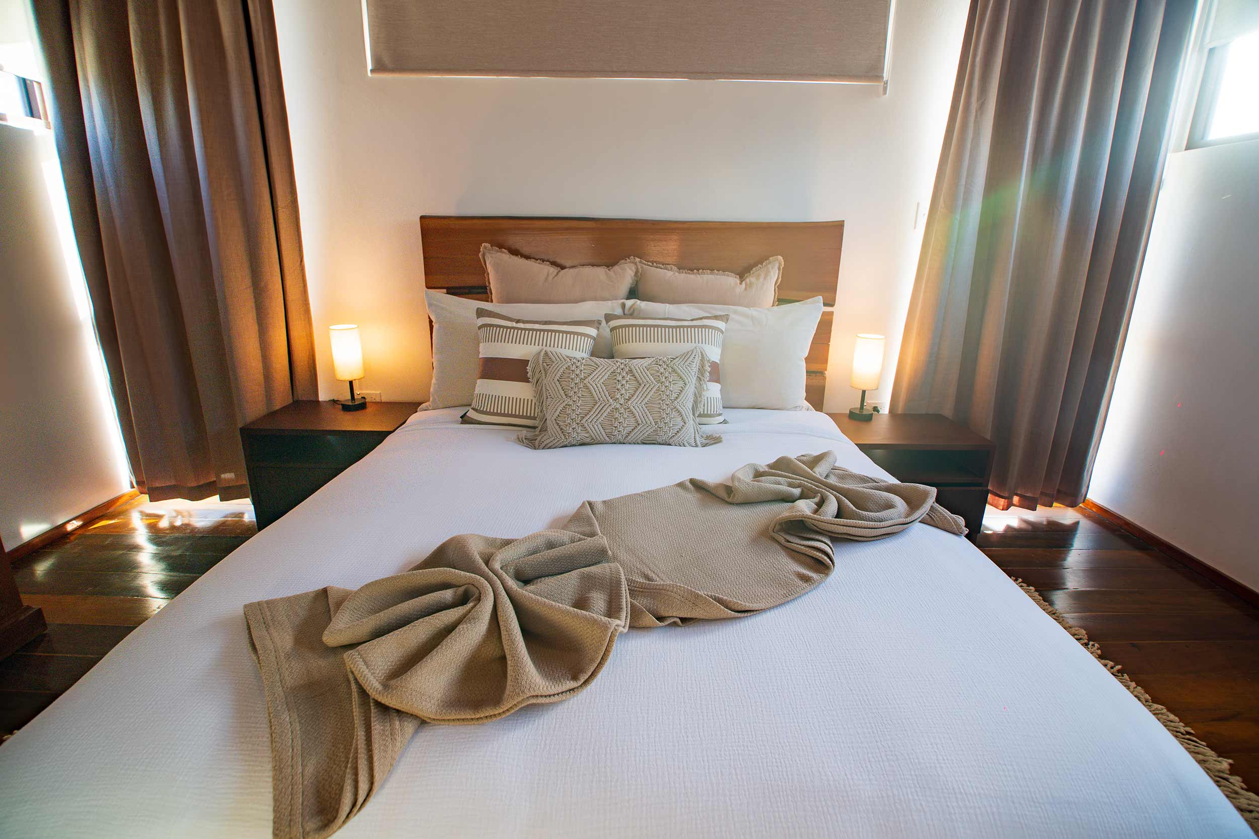 Cozy bedroom with wooden bed frame, decorative pillows, and towel arrangement on white linens.