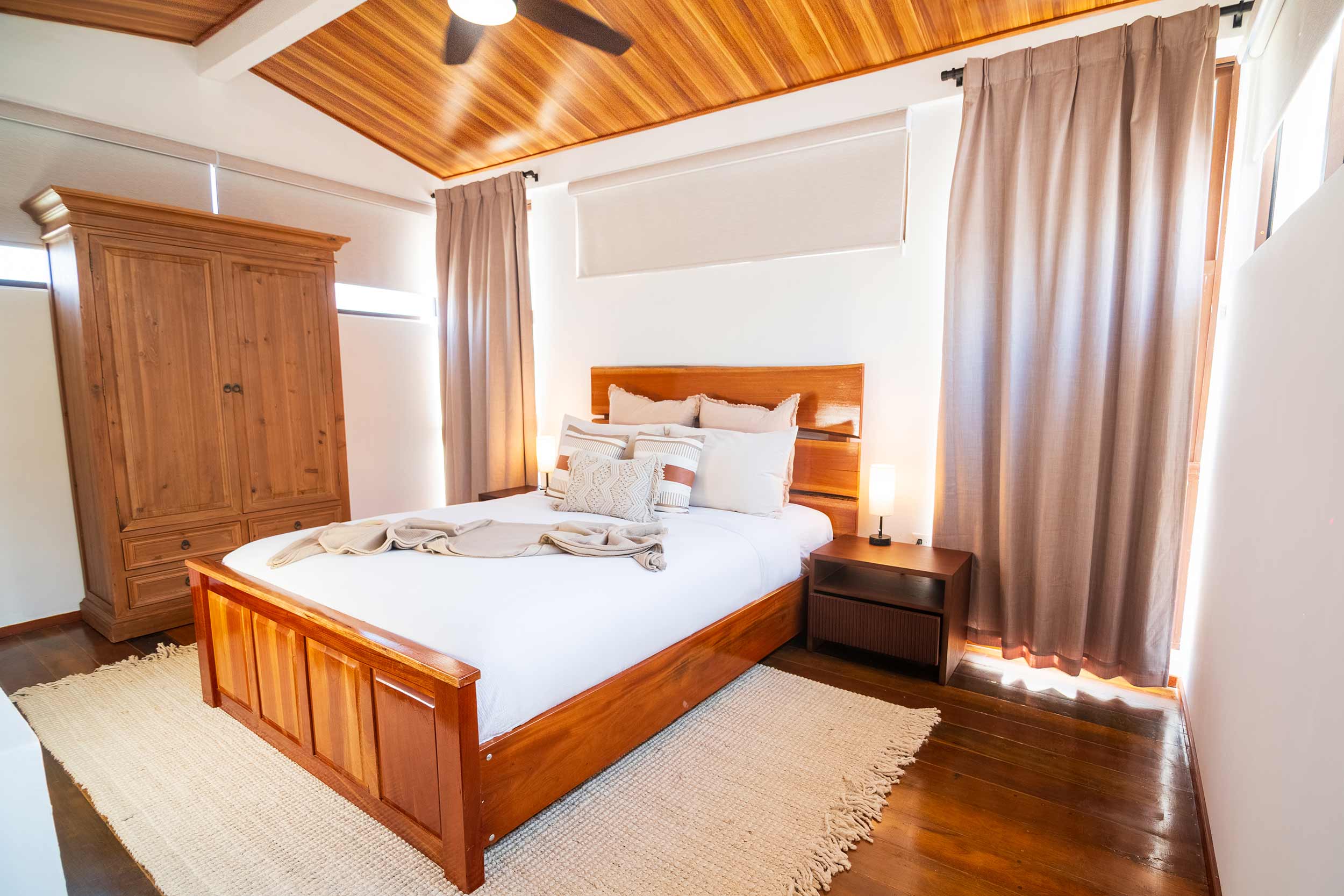 Elegant bedroom with wooden ceiling, king bed, bedside lamps, and neutral decor.
