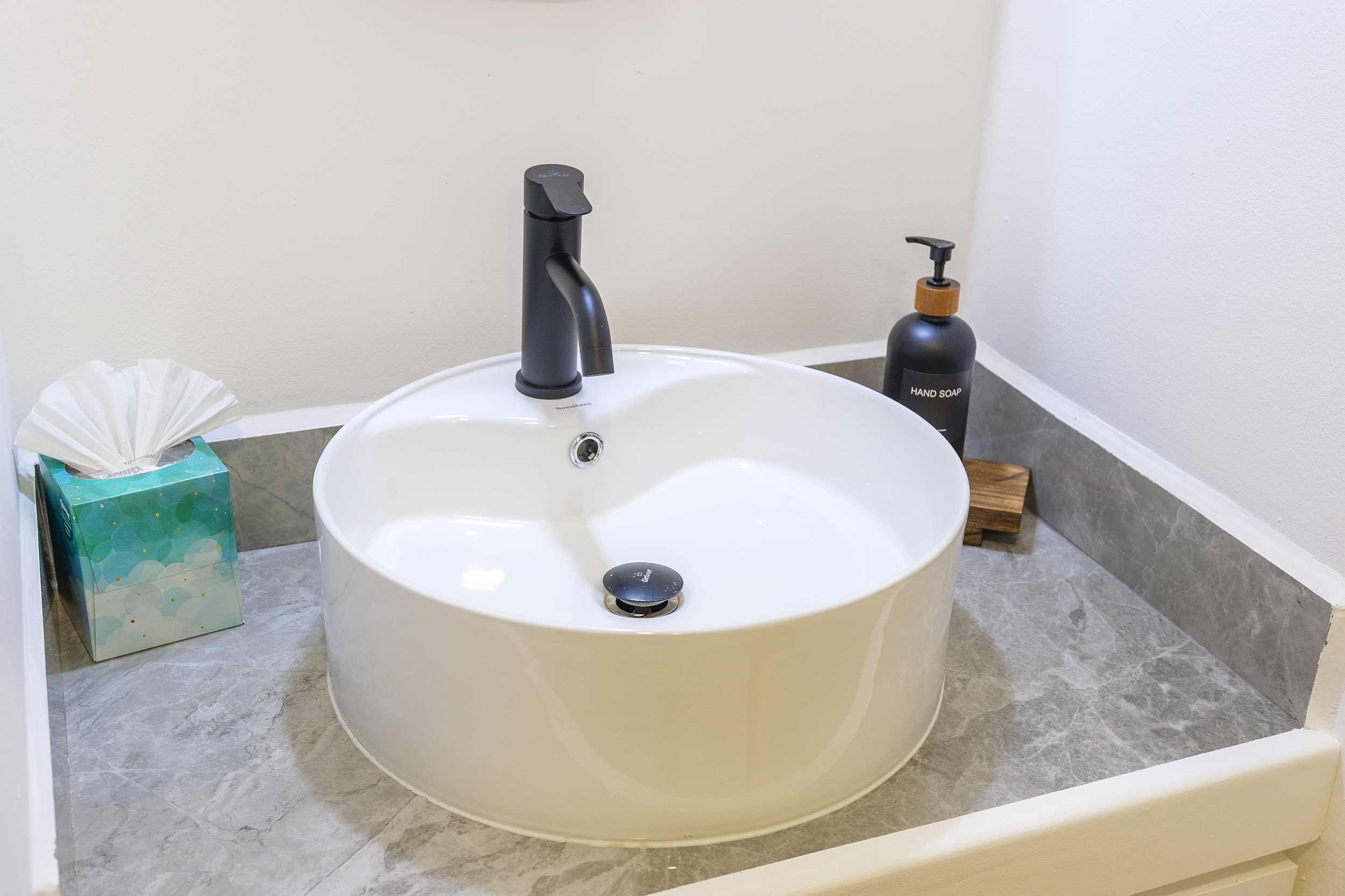 Modern bathroom sink with matte black faucet, hand soap, and marble countertop.
