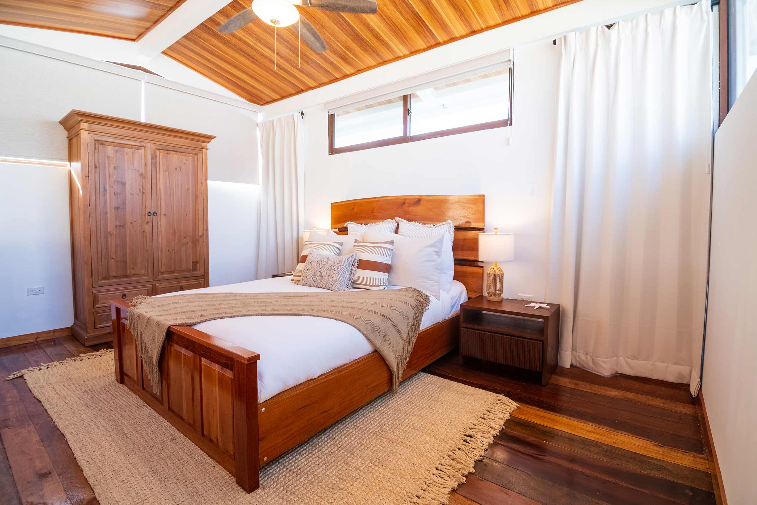 Spacious bedroom with wooden ceiling, king bed with neutral linens, and wooden wardrobe.