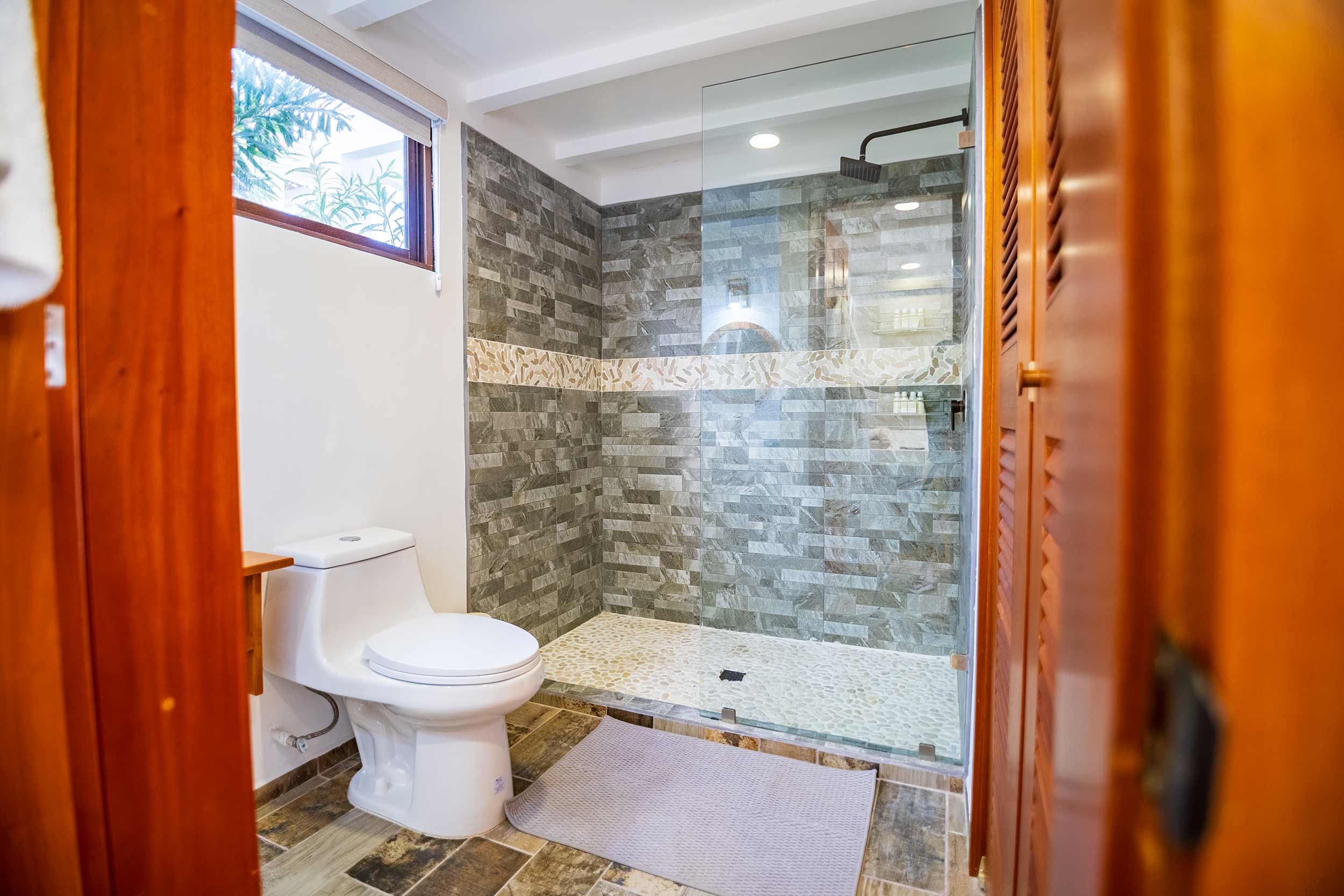 Modern bathroom with glass walk-in shower, stone tile walls, and window for natural light.
