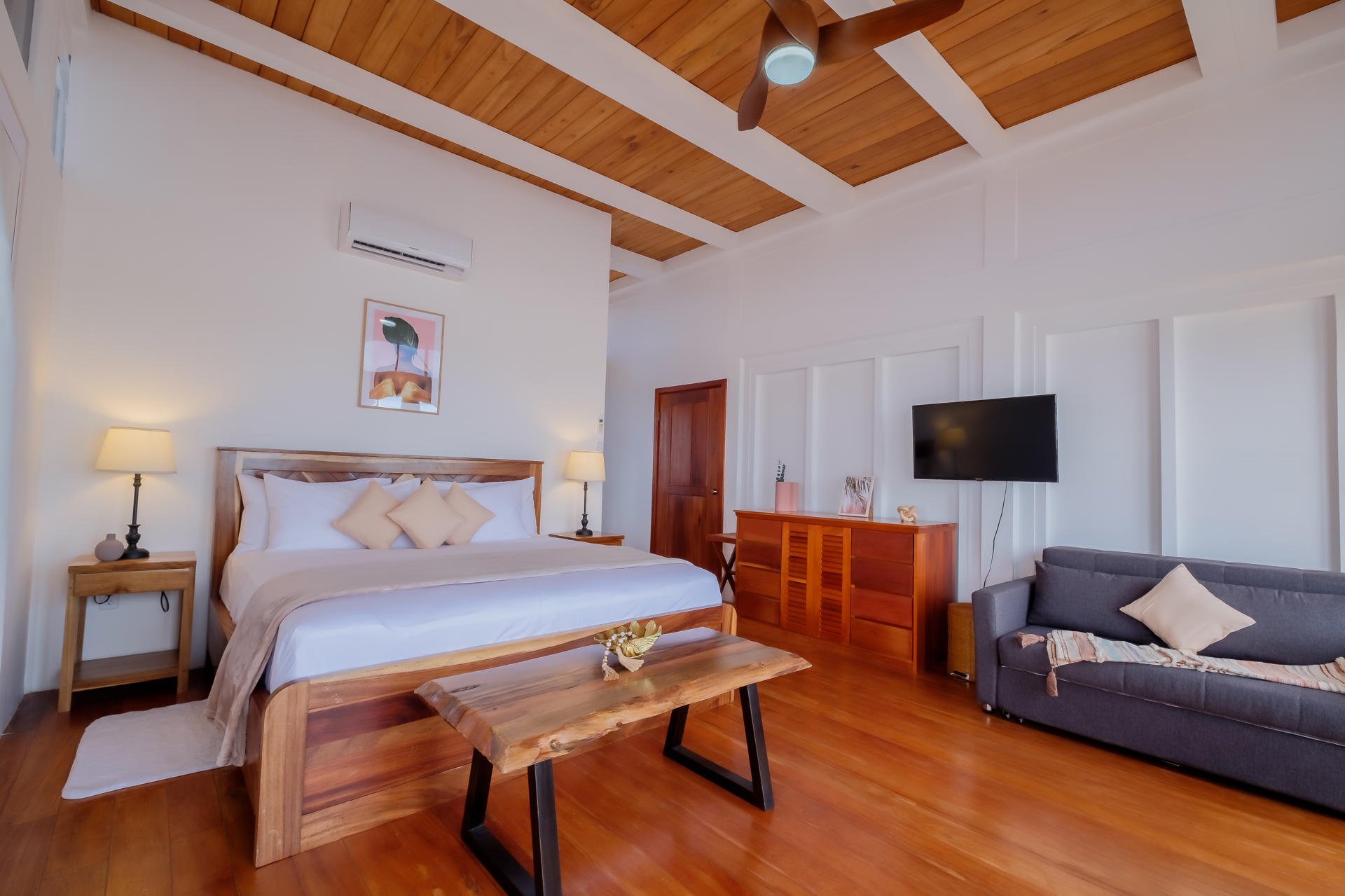 Spacious villa bedroom with a wooden king bed, neutral decor, and woven wall art in a bright, airy interior.