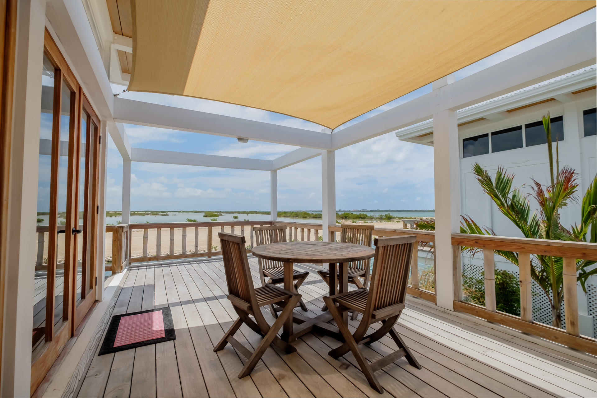 Bright villa living area with round glass dining table, wooden staircase, and TV lounge space.
