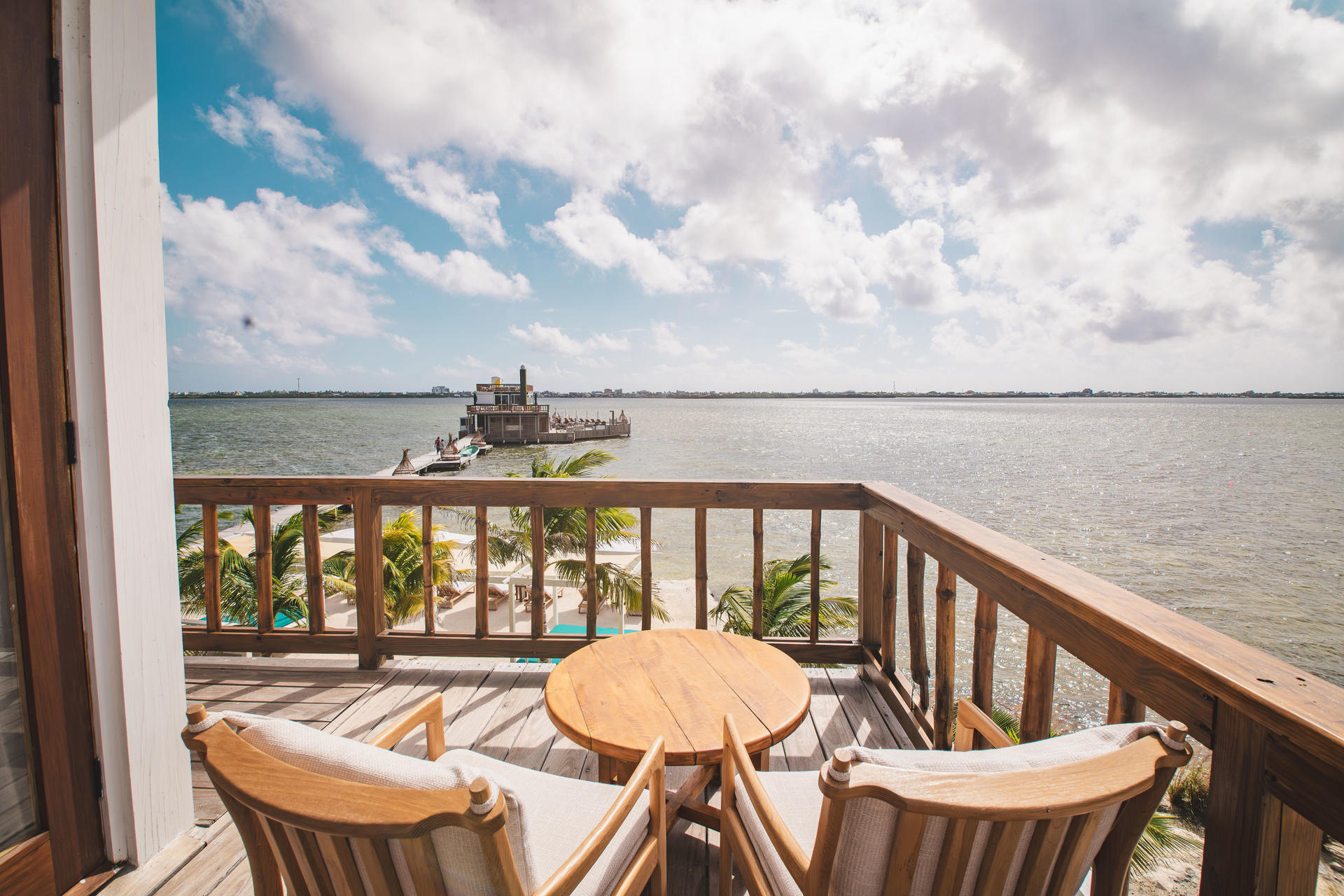 Villa balcony with wooden railing and lounge chairs overlooking coastal water and mangroves.
