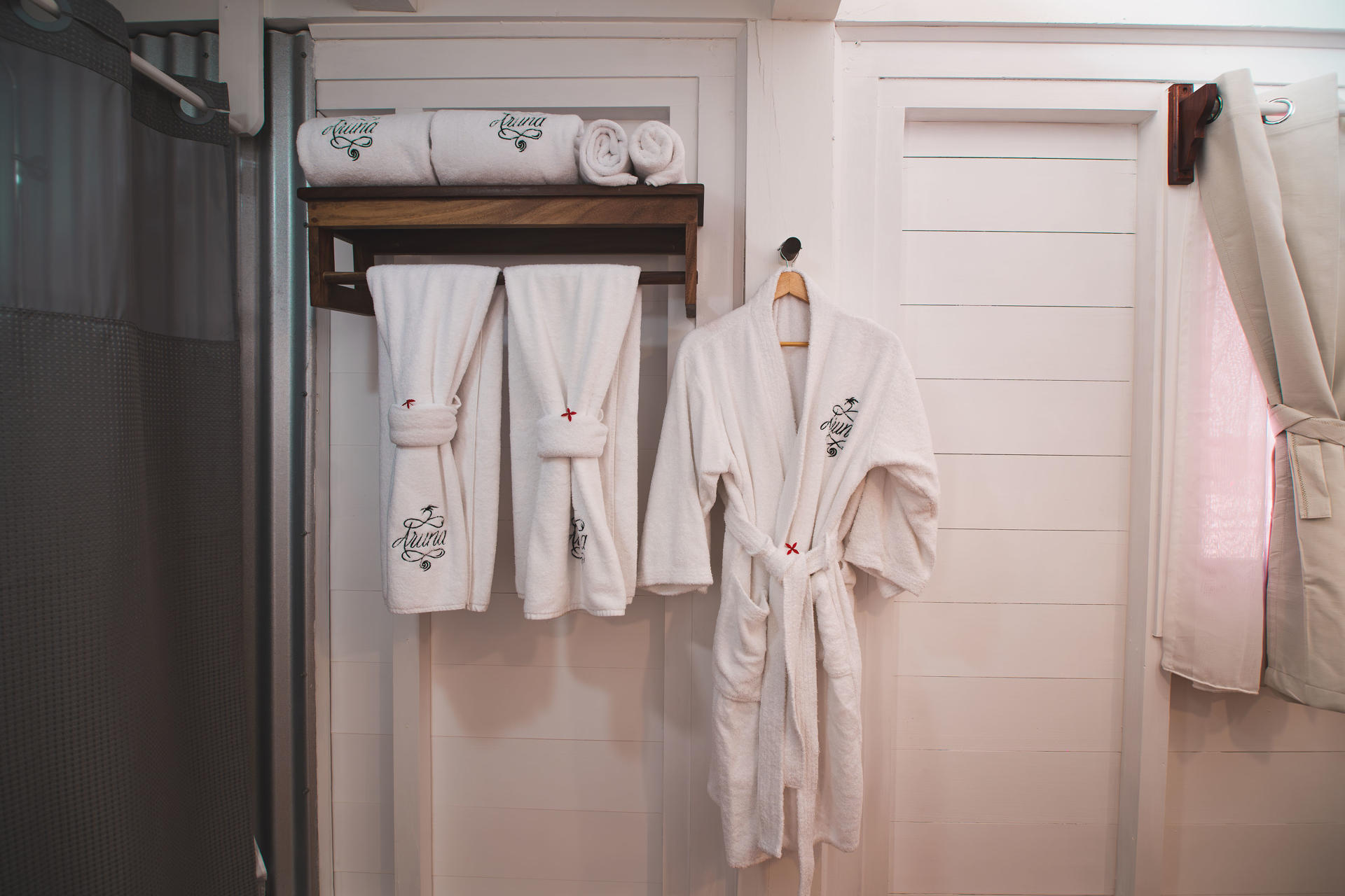Villa bathroom with white vanity sink, round mirror, wooden doors, and hanging bathrobe.
