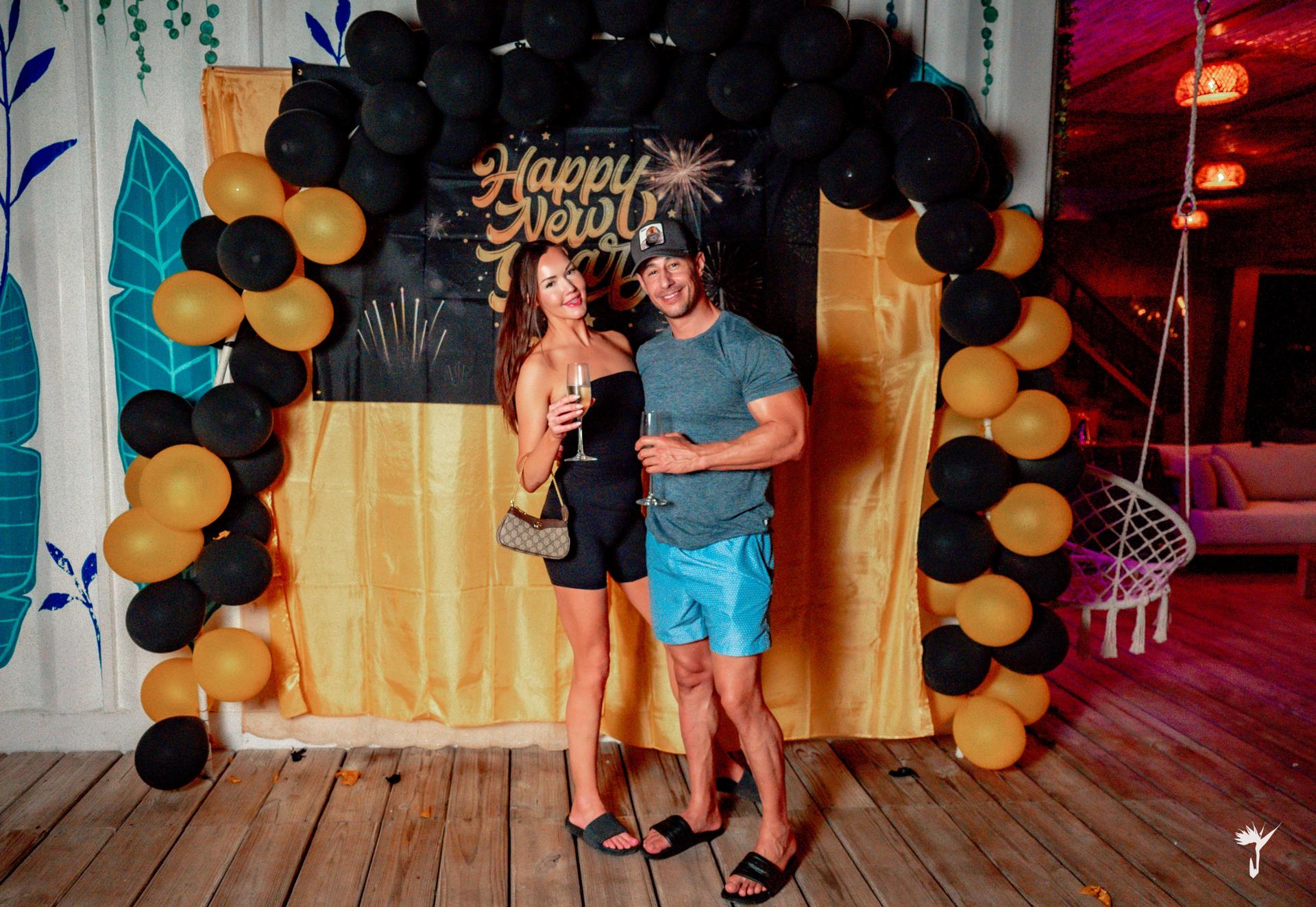 Couple toasting with champagne at the Happy New Year photo backdrop at Aruna