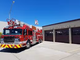 Red fire truck parked outside a fire station with closed garage doors under a clear blue sky.