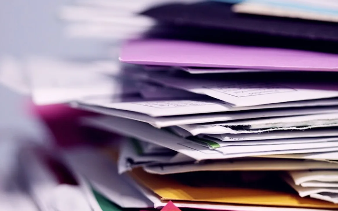 Close-up of a thick, disorganized stack of papers and folders in various colors.