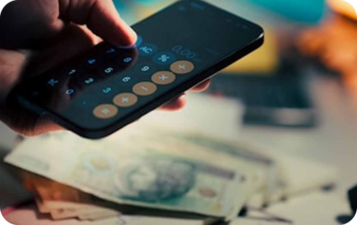 Hand using a smartphone calculator app with various paper currencies blurred in the background.