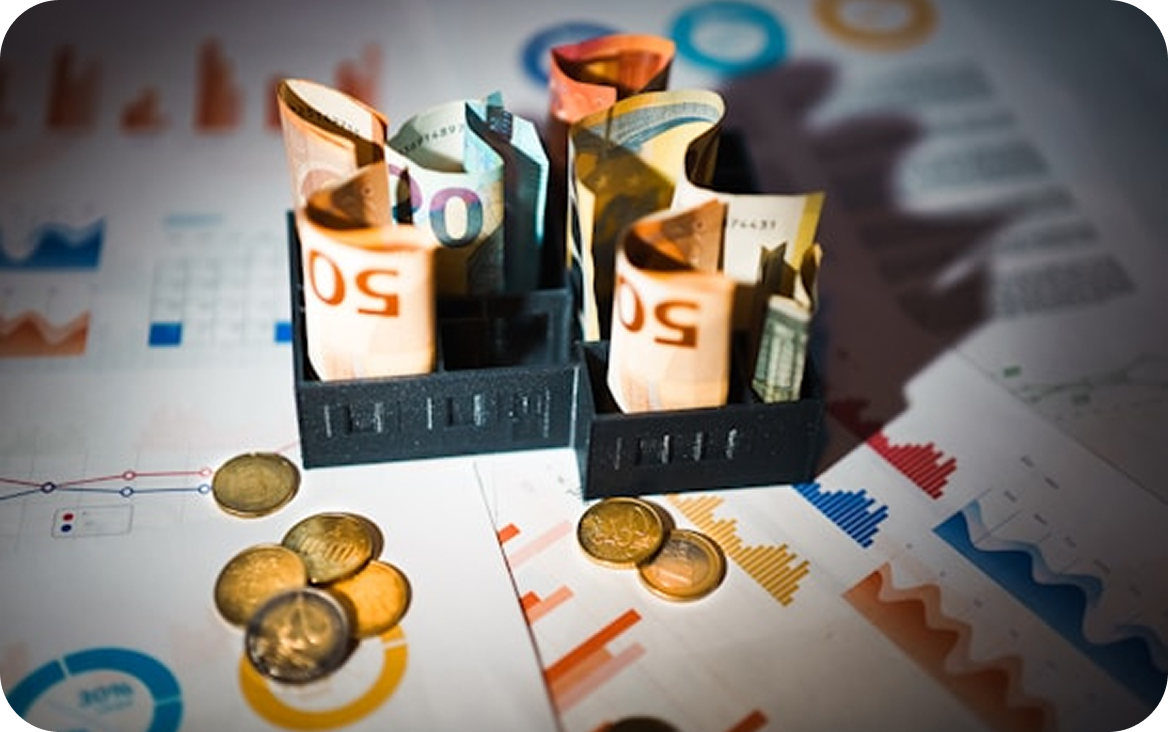Folded euro banknotes placed upright in two black holders on top of financial charts with scattered euro coins around.