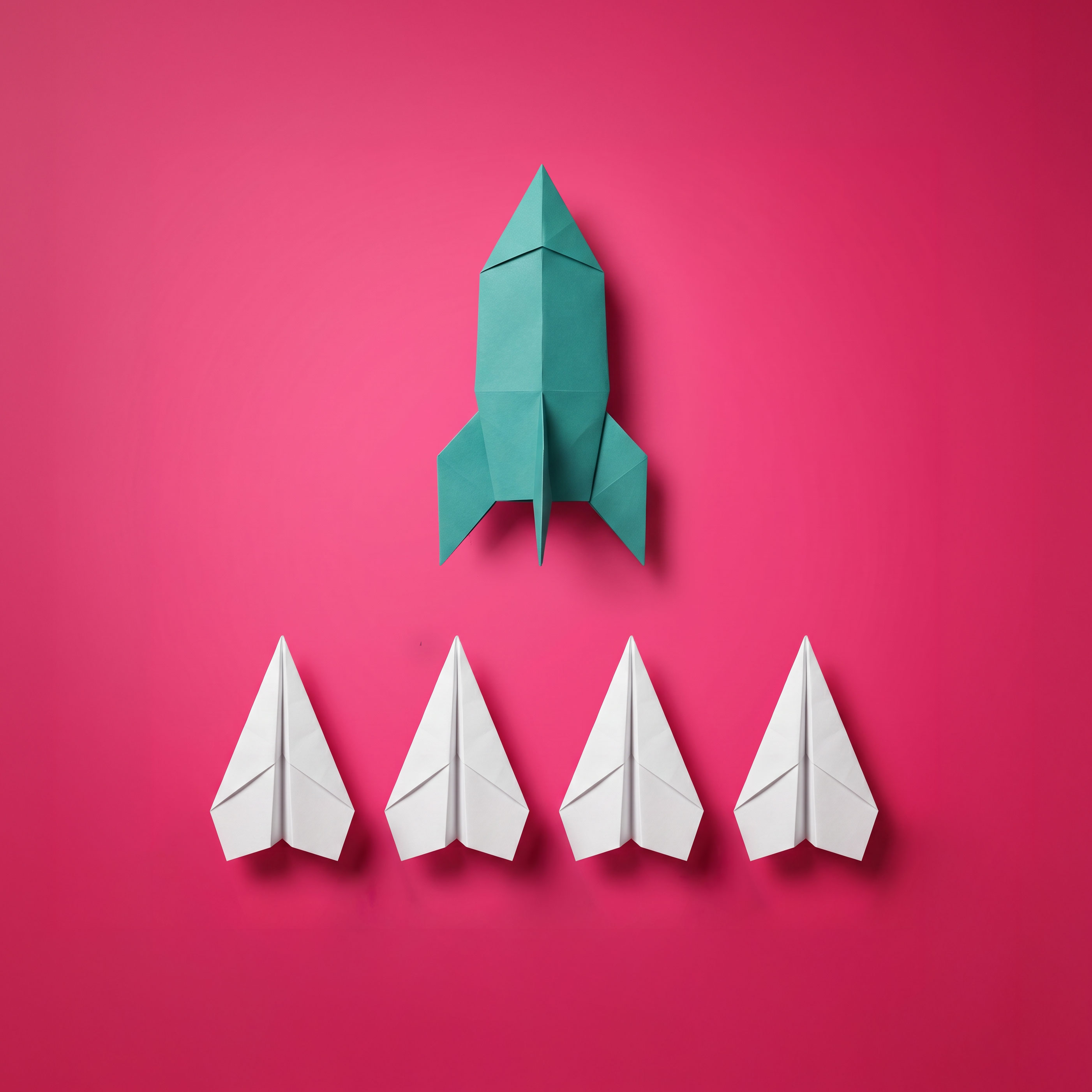 One large green paper rocket above four smaller white paper airplanes arranged in a row on a bright pink background.