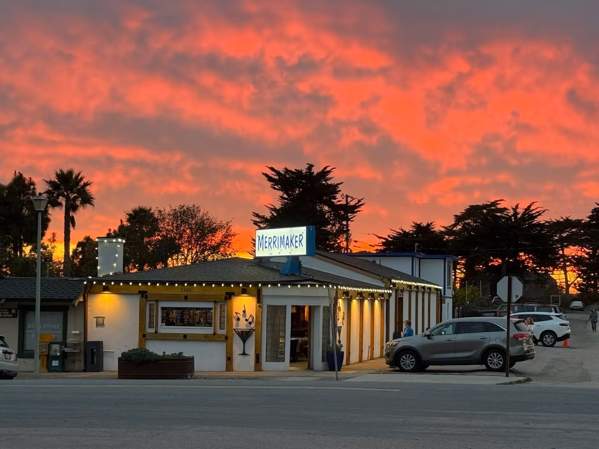 A sunset view of Niffy's Merrimaker with several cars parked in front, casting long shadows on the pavement.