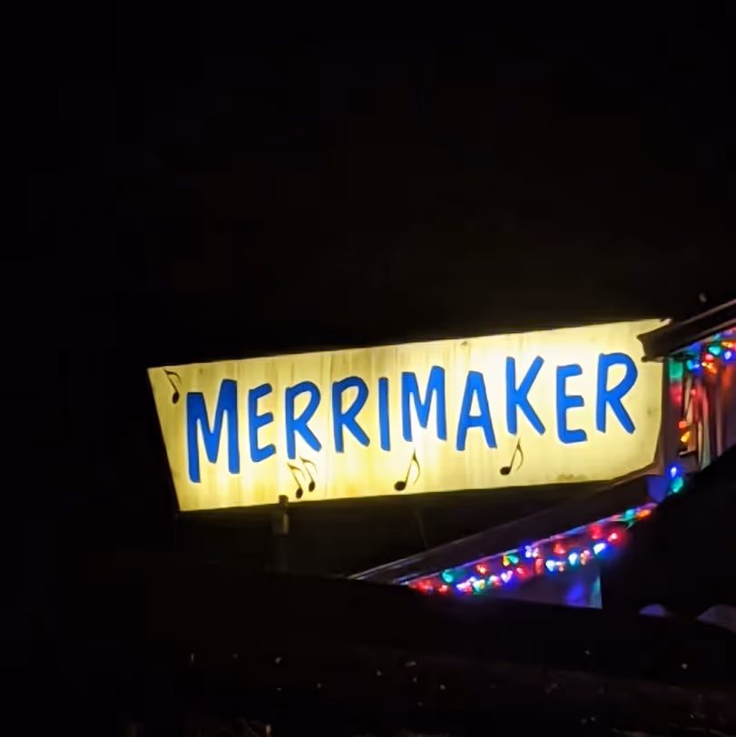 A nighttime view of a building sign reading "Merrimaker," illuminated against the dark sky.