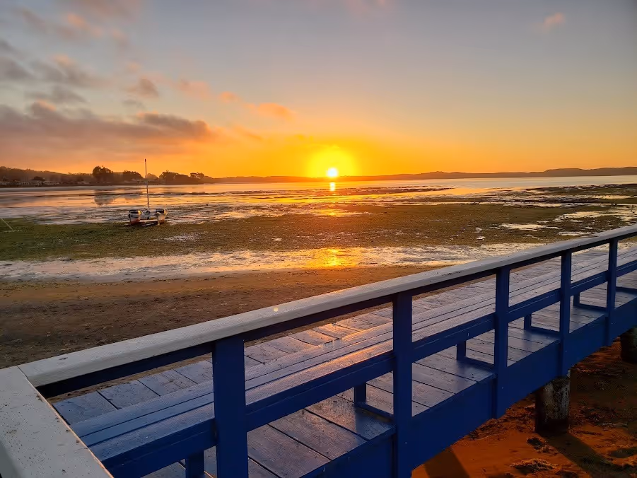 A blue wooden bridge spans a tranquil body of water, illuminated by the warm hues of sunset.