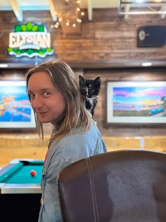 A woman with long hair and a black and white cat on her back.