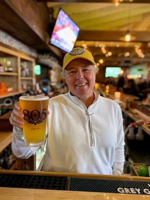 A woman wearing a yellow hat holding a glass of beer.