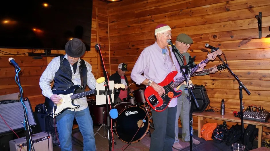 A band performs on a bandstand in a wooded area, surrounded by trees and nature, creating a lively outdoor atmosphere.