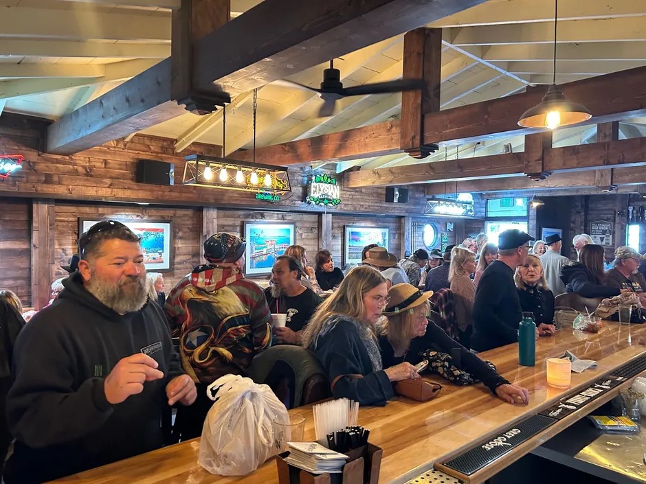 A lively crowd of people socializing at a bar inside a bustling restaurant.
