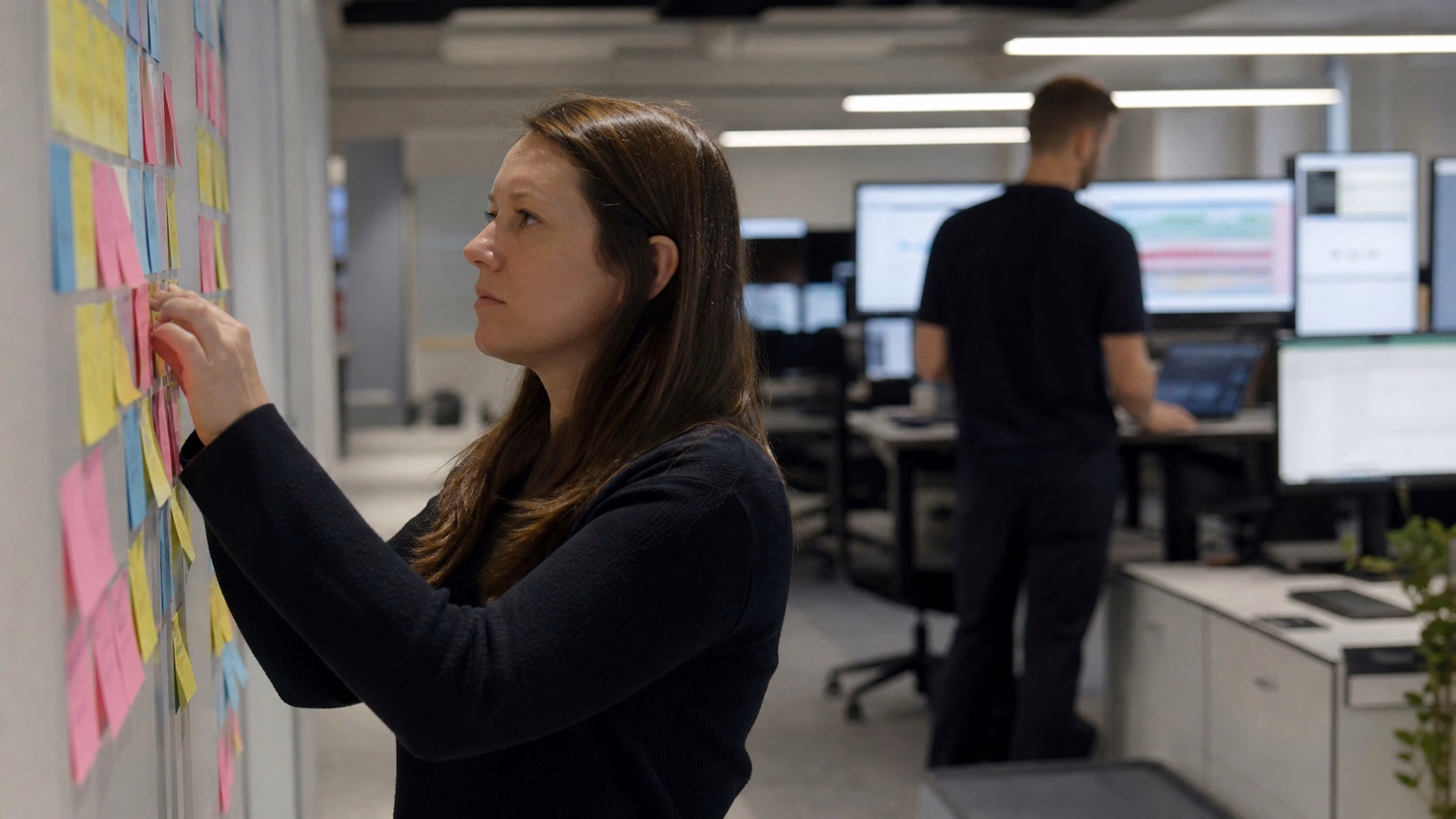 Woman organizing sticky notes on wall, cybersecurity assessment 68 chars
