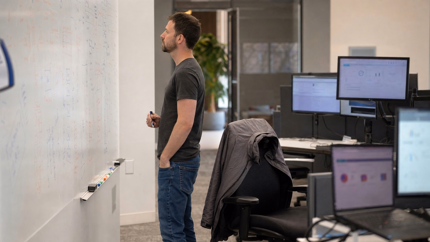 IT consultant strategizing at whiteboard with markers, jacket nearby