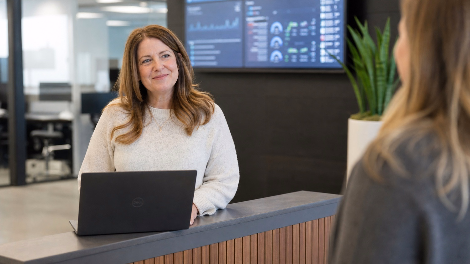 Receptionist at desk with open laptop, looking off-camera