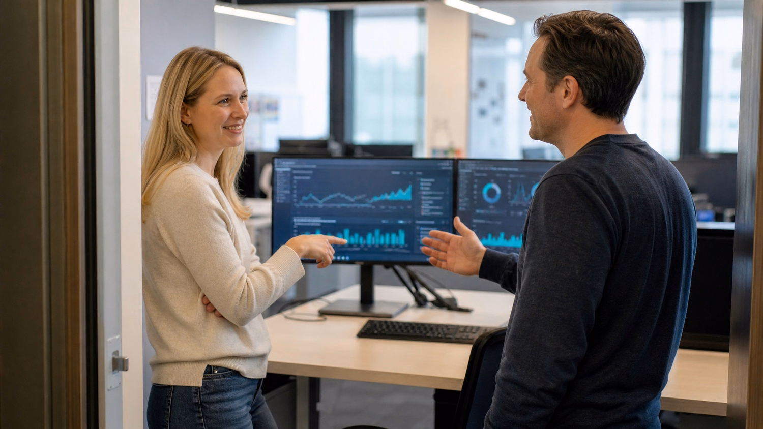 Colleagues discuss monitor display in office doorway
